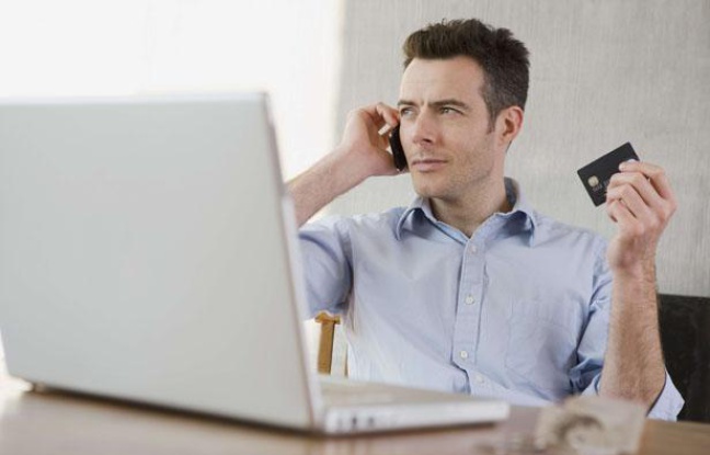 Un homme tient une carte de crédit et consulte son ordinateur portable Un homme tient une carte de crédit et consulte son ordinateur portable
