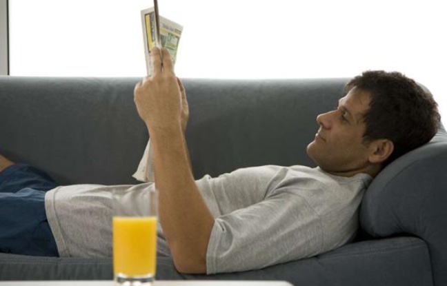 Un homme lit le journal sur son canapé. Un homme lit le journal sur son canapé.