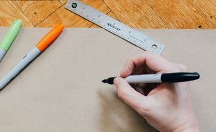 Illustration d'une personne face à une feuille de dessin, avec des marqueurs et une règle