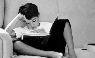 Un enfant lit un livre chez lui.