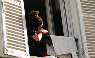 Une personne regarde par la fenêtre en période de confinement.