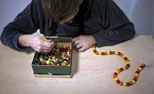 Une personnes autiste réalise un collier de perles avec l'aide du personnel du centre médical