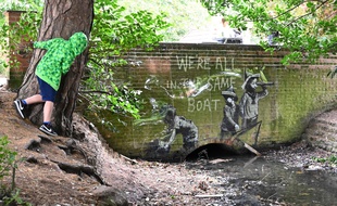 Banksy a réalisé une peinture au pochoir de trois enfants sur une barque de tôle ondulée reposé contre un mur de briques, avec l’inscription « We’re all in the same boat », faisant écho à la crise environnementale.