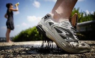 Une personne marche sur l'asphalte qui a commencé à fondre pendant qu'une femme boit, le 23 juillet 2006, à Givors, près de Lyon, dans le sud-est de la France. (Photo illustration)