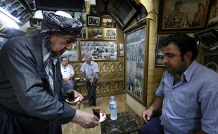Mam Khalil, 76 ans, sert un client de son café, le 12 mai 2014 à Erbil, la capitale de la région autonome kurde du nord de l'Irak, devant les galeries de photos retraçant l'histoire du pays qui tapissent les murs