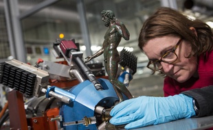 Une scientifique place une statuette de bronze pour analyse devant Aglaé.
