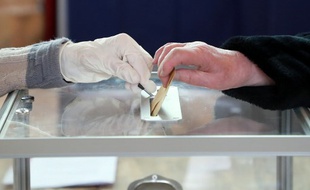 Un assesseur, portant des gants en latex, tient la fente de l'urne ouverte pendant qu'un électeur y glisse son enveloppe dans un bureau de vote au Touquet, dans le nord de la France, le 15 mars 2020, lors du premier tour des élections municipales.
