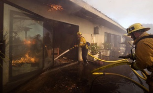 Des pompiers en train d'éteindre un incendie dans le quartier de Bel-Air, à Los Angeles