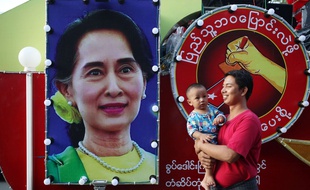 Un homme et un bébé passent devant une affiche à l'effigie d'Aung San Suu Kyi, le 8 novembre 2015 à Mandalay, en Birmanie.
