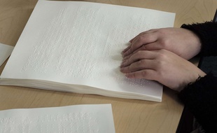 Une personne handicapée déchiffre une feuille de braille.