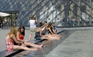 Des touristes se rafraichissent dans un bassin devant la pyramide du Louvre à Paris, le 3 juillet 2014