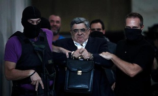 Nikos Michaloliakos entouré de policiers masqués à la sortie des locaux de la police le 28 septembre 2013 à Athènes