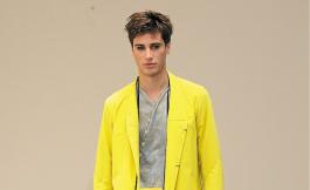 De gauche à droite :Veste à boutons en toile de coton jaune acide, chemise en popeline de coton et soie grise, pantalon droit en maille de coton kaki. Gustavo Lins. Imperméable en toile de coton jaune acide, tee-shirt en jersey de coton imprimé « dripping » sable d'or, pantalon droit en toile de coton sable. Collier-pochette en cuir surpiqué jaune acide.