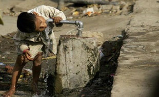 Un enfant boit de l'eau au robinet, en Inde, dans un quartier où l'eau potable n'arrive pas dans les maisons.