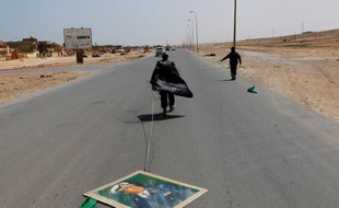 Un rebelle traine un portrait du leader libyen Mouammar Kadhafi sur une route à Bin Jawad, Libye, le 28 mars 2011.