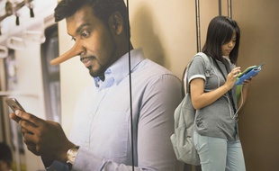 Photo d'illustration sur les fausses informations - En Malaysie, une femme consulte son téléphone portable devant une affiche d'une campagne contre les «fake news» en mars 2018.