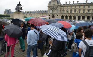 Des visiteurs font la queue sous la pluie devant le musée du Louvre à Paris le 8 août 2014