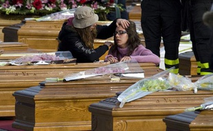 Une femme agenouillée devant un cercueil pendant les funérailles d'Etat des victimes du séisme, à l'Aquila.