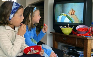 Deux petites filles regardent la télévision en mangeant des sucreries, le 8 octobre 2003 à Rennes.