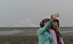 Des touristes prennent des selfies le 28 mars 2016 devant le volcan de boue qui a dévasté Sidoarjo sur l'île de Java, en Indonésie