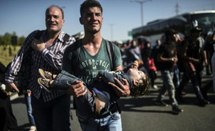 Un homme porte un enfant en train de dormir dans le cortège de plusieurs centaines de migrants qui marchent vers la frontière entre la Grèce et la Turquie, le 18 septembre 2015 près de la ville turque d'Edirne