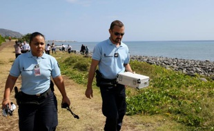 Des policiers portent dans une boîte des débris métalliques découverts sur une plage de Saint Denis, à La Réunion, le 2 août 2015