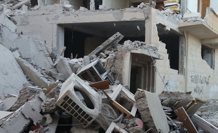 People walk past a building that was reportedly targeted by the US-led coalition, in the Islamic State (IS) controlled Syrian city of Raqqa on November 11, 2014. The leader of the moderate Syrian opposition accused the US-led coalition in an interview of having a "confused" strategy in Iraq and Syria that targeted jihadists but turned "a blind eye" to crimes by Syrian President Bashar al-Assad. AFP PHOTO/RMC/STR