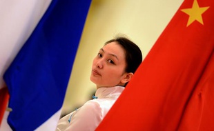 Une femme se tient entre un drapeau français et un drapeau chinois lors d'une cérémonie pour le 50e anniversaire des relations diplomatiques franco-chinoises, à Pékin le 27 janvier 2014.