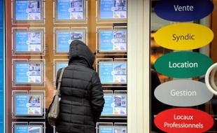 Une femme regarde les annonces dans la vitrine d'une agence immobilière