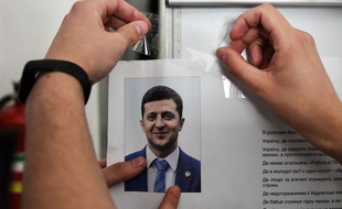Un membre d'une commission locale pour les élections en Ukraine affiche un portrait du comédien Volodymyr Zelensky favori des sondages pour le second tour de l'élection présidentielle en Ukraine dimanche 21 avril 2019.