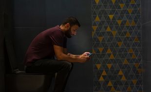 Un homme aux toilettes avec son portable.