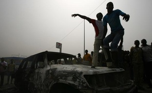 Des étudiants pro-Gbagbo sur un véhicule des Nations unies brûlé le 13 janvier 2011, à Abidjan, en Côte d'Ivoire.