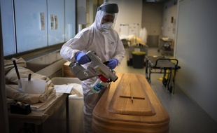 Un employé de morgue désinfecte un cercueil contenant le corps d'une personne décédée du COVID-19 avant des funérailles à la morgue Memora de Gérone, en Espagne, le jeudi 4 février 2021.