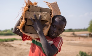 Un enfant transportant des briques au Soudan du Sud.