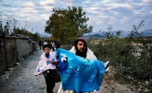 Un homme porte son enfant alors qu'il vient avec d'autres migrants de passer la frontière gréco-macédonienne près de Gevgelija, en Macédoine, le 15 novembre 2015