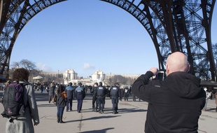 Un touriste prend une photo sous la tour Eiffel, alors qu'une patrouille de police s'éloigne, le 17 janvier 2015.