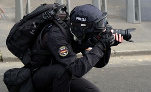 Une personne vêtue de noir avec une casquette siglée presse prenant des photos, le 20 avril 2019 à Paris lors d'une manifestation de