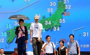 Des passants devant un écran diffusant la météo à Tokyo, le 21 juillet 2018.
