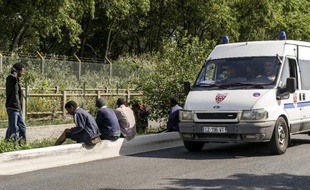Un véhicule de CRS passent devant des migrants près de la "Jungle", cette zone de Calais où nombre d'entre eux campent en attendant un passage vers l'Angleterre, le 5 août 2014