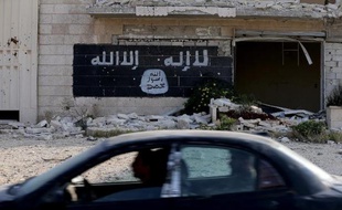 Une voiture passe devant les ruines d'une usine, dont le mur a été peint aux couleurs d'un groupe djihadiste, le 18 novembre 2014, à Alep en Syrie