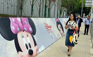 Des Chinois marchent devant une bannière publicitaire pour le premier magasin Disney de Chine, à Shanghai, le 20 mai 2015.