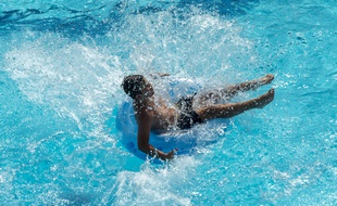 Un jeune nageur saute avec sa bouée dans une piscine (image d'illustration).