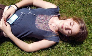 Une jeune fille écoute de la musique au casque, dans l'herbe, à la cool.