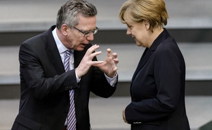 Le ministre allemand de l'Intérieur Thomas de Maiziere (L), en discussion avec la chancelière allemande Angela Merkel lors d'une session plénière à la Chambre basse du Parlement le 3 juillet 2014 à Berlin avant que les législateurs allemands votent un projet de loi pour un salaire minimum national.