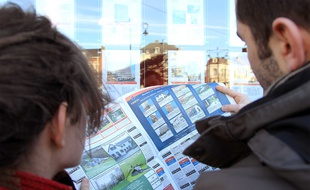 Jeune couple à la recherche d'un bien immobilier, consultant les annonces d'une agence.