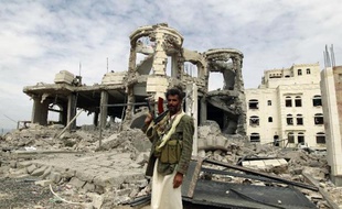 Un milicien Houthi pose devant une maison détruite par un bombardement aérien, le 29 mai 2015 à Sanaa