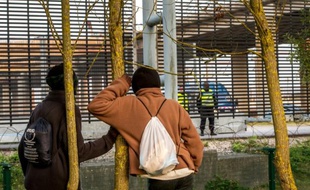 Deux migrants du Darfour Guli (G) et Mamadou (D) regardent des policiers surveillant l'Eurotunnel à Coquelles le 31 juillet 2015