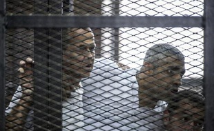 Les journalistes australien Peter Greste (g), canado-égyptien Fadel Fahmi (c) et égyptien Baher Mohamed écoutent la sentence prononcée contre eux depuis le box des accusés au tribunal de police du Caire, le 23 juin 2014