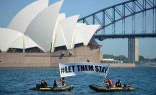 Des militants de Greenpeace brandissent une banderole avec l'inscription "#LET THEM STAY" ("#Laissez les rester") devant l'opéra de Sydney, le 14 février 2016, alors qu'un hôpital australien refuse de renvoyer un bébé dans un camp de réfugiés controversé