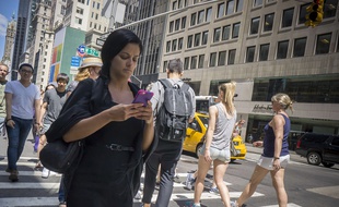 Une passante consulte son téléphone en traversant la rue à New York.